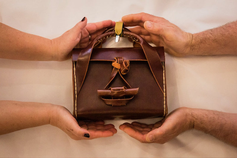 A finished handmade leather bag cradled in the maker's hands